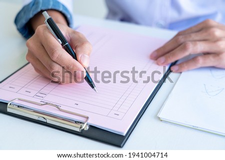 business man works on the table holds pen in right hand and write data in the table chart, wear a white and blue shirt.