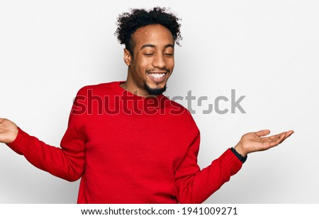 Young african american man with beard wearing casual winter sweater smiling showing both hands open palms, presenting and advertising comparison and balance 