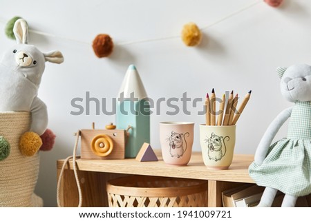 Stylish scandinavian newborn baby room with toys, plush animal, photo camera and child accessories. Cozy decoration and hanging cotton balls on the white wall. Copy space.