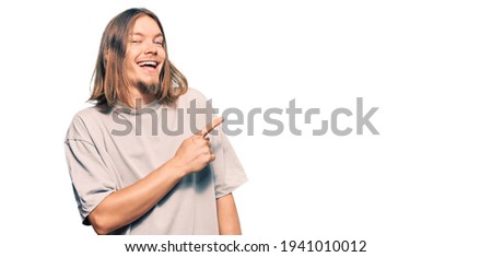 Handsome caucasian man with long hair wearing casual clothes cheerful with a smile of face pointing with hand and finger up to the side with happy and natural expression on face 