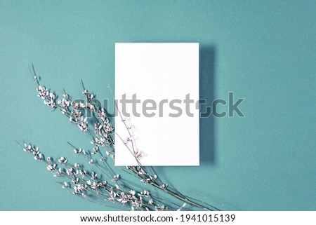 White paper empty blank, flowers on blue background. Invitation card mockup on white table. Flat lay, top view, copy space, mock up