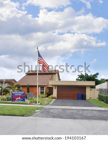 American Flag pole sold real estate (another success let us help you buy sell your next home) sign Suburban home Residential Neighborhood USA Blue sky clouds