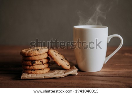 cookies with chocolate chips and a cup with a hot drink on a wooden table.