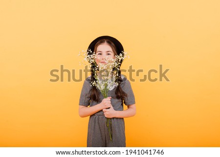 Portrait of cute little girl with flower bouquet in the studio on yellow background. Congratulation, spring or happy holiday concept. Copy space for text