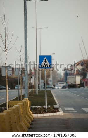 A vertical shot of a road sign of a pedestrian walkway with white traffic marking 