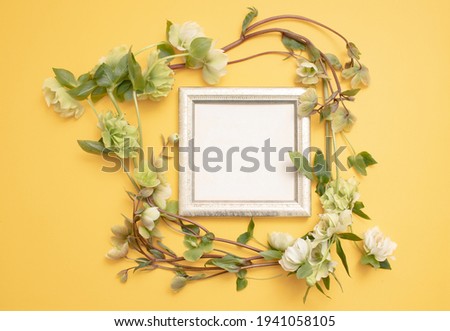 Flat lay composition of the beautiful empty antique frame, decorated with ranunculus flowers, on the textured yellow wall. Copy text for a menu, reception, party poster, or wedding invitation. 