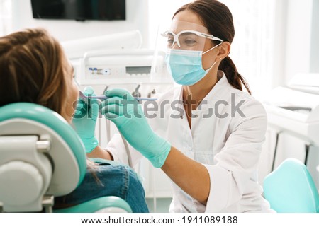 European mid pleased dentist woman in face mask working in dental clinic Royalty-Free Stock Photo #1941089188