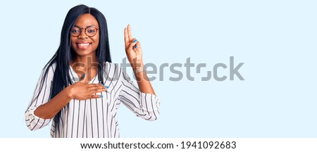 Young african american woman wearing casual clothes and glasses smiling swearing with hand on chest and fingers up, making a loyalty promise oath  Royalty-Free Stock Photo #1941092683