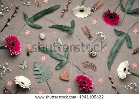 Jungle floral flat lay on linen textile. Bold tropical plant mix with dark red, burgundy and white gerbera flowers, feathers, quail eggs. Springtime floral flat lay with exotic fern leaves.