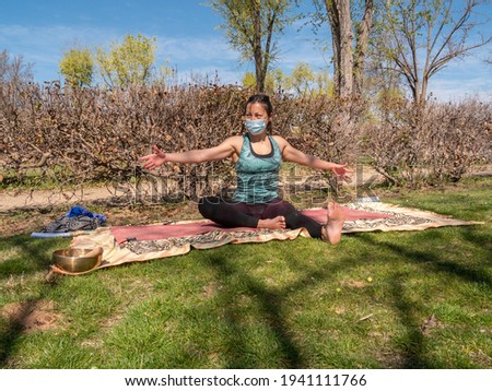 Brunette woman doing yoga class in a park, on a sunny day and wearing a virus mask.