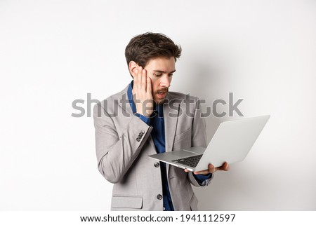Shocked and worried businessman making mistake on laptop, looking at computer upset, standing on white background