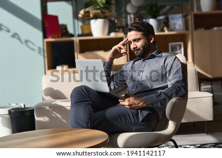 Indian business man executive working on laptop sitting on chair in modern office. Eastern male entrepreneur using computer remote studying, virtual training, watching online education webinar. Royalty-Free Stock Photo #1941142117