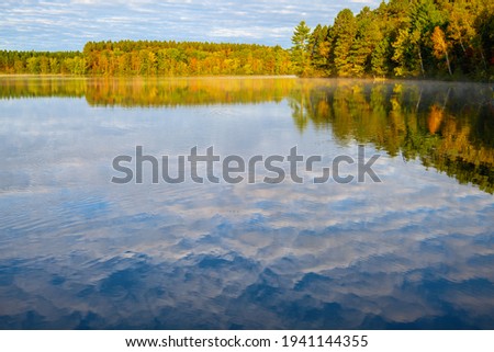 Fall Autumn colored trees reflection in Lake. Puffy White clouds reflection
