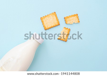 Broken dry cookies and bottle of milk on blue background, top view, lay out. Concept picture about food and breakfast