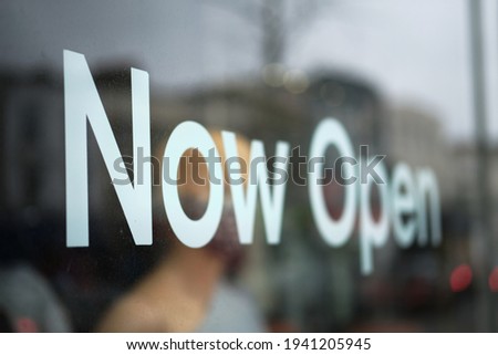 Close-up of a display window of a small business with the words: Now Open after easing the restriction.