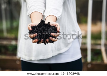 Young woman's hands holding fresh compost with blurred raised beds in a garden. 