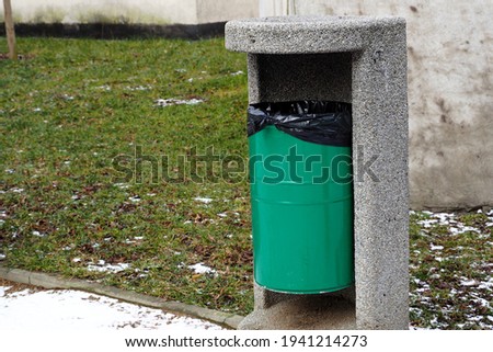 green metal garbage can stands in the park on a spring day side view