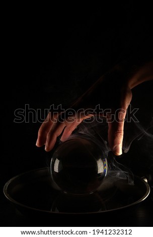 A hand over a black glass ball with smoke around it