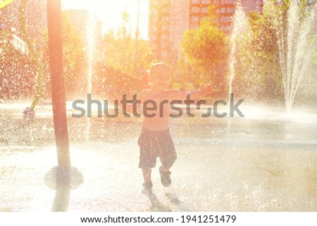 Happy child has fun playing in water fountains on hot day during summer. Boy playing in water at waterpark. A kid in spray park.