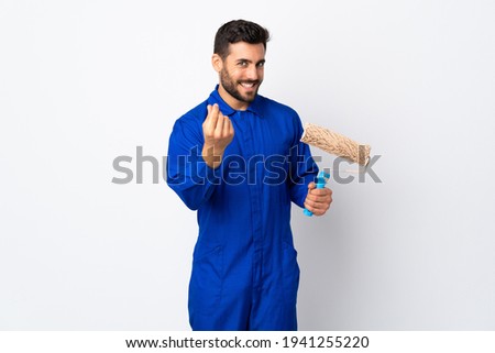 Painter man holding a paint roller isolated on white background making money gesture