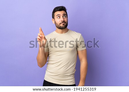 Young handsome man with beard over isolated background with fingers crossing and wishing the best