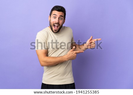 Young handsome man with beard over isolated background surprised and pointing side