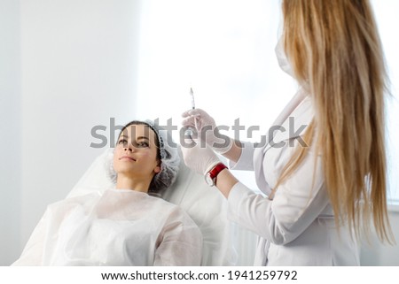 Attractive young woman is getting a rejuvenating facial injections. She is sitting calmly at clinic. The expert beautician is filling female wrinkles by hyaluronic acid. High quality photo