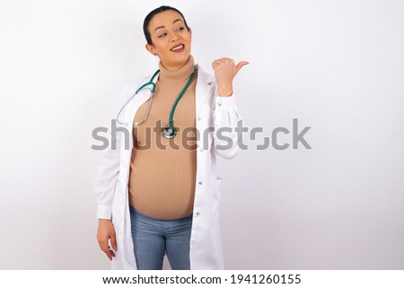 Charming young pregnant doctor woman wearing medical uniform against white background looking at copy space having advertisements