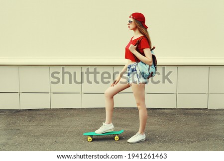 Young woman with green skateboard wearing a shorts and red baseball cap in a city