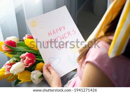 Child's drawing greeting card with words Happy Mother`s Day and bouquet of flowers colorful tulips in mother`s hands. Lifestyle celebration or surprise for Mom on Mother`s Day.