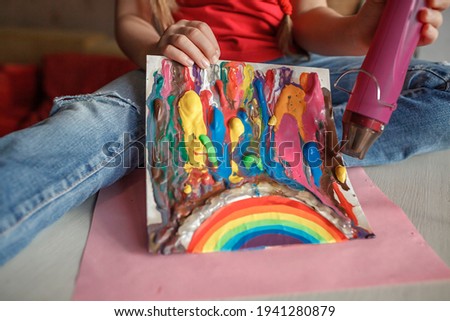 School girl drawing rainbow with melted crayon pencils, she using blow dryer and wax stars to melt, abstract art for kids with, original idea for social media campaign for coronavirus prevention