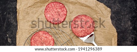 Ground Beef Patties for Grilling and Roasting. Raw Minced Steak Burgers from Beef Meat on Black Background. BBQ Grill Tools with Raw Beef Hamburger Patties. Burger Cutlets On Paper And Grill Grate.