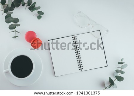 Flatlay desk table. Workspace with modern pink macarons, cup of coffee and green leaves eucalyptus on white table. Copy space, top view. Feminine concept