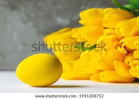 Bouquet of bright yellow tulips and Easter eggs lying on white wooden surface on gray background, copy space