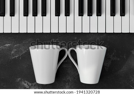 Keyboard of a piano with two white mugs in front of it on black background