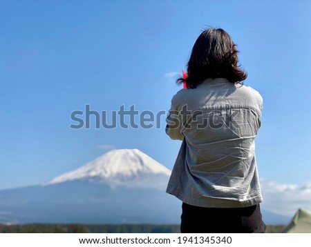 Back view of a woman shooting Mt. Fuji with a smartphone at a campsite