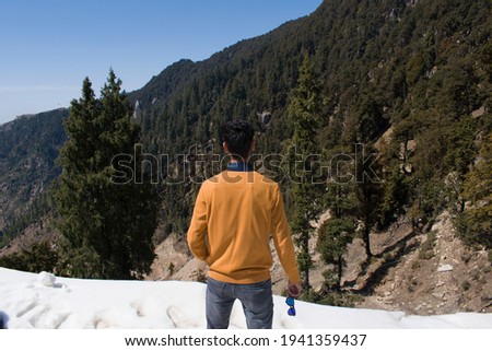 picture of boy's back standing on snow with style holding sunglasses in right hand.