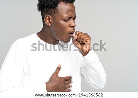 Sick African American man strongly coughing. Black man feeling unwell, suffered from asthma, flu, allergy, bronchitis, tuberculosis, virus, touching her chest, isolated on studio grey white background Royalty-Free Stock Photo #1941366562