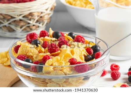 Glass bowl with cereal flakes and berries and milk on the table, close-up. Healthy summer breakfast