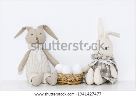 Easter composition with soft toys of hares and white eggs that are on the shelf in the room