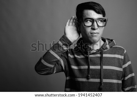 Young Asian nerd man wearing hoodie against gray background