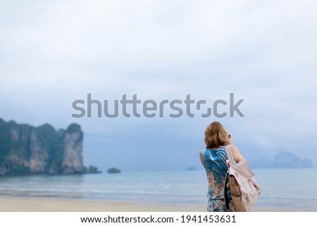 Traveler and photographer pretty woman in long dress is taking photo of tropical seascape on beautiful ocean beach. Local solo isolation tourism. Scenic photo with copy space