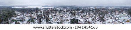 Panoramic aerial view of a snow-covered village near the lake. Winter rural landscape. Top view of houses and trees. Cold snowy winter weather. Snow on the roofs. Toksovo, Leningrad region, Russia.