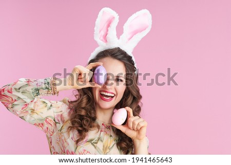young woman in floral dress with bunny ears and easter egg isolated on pink background.