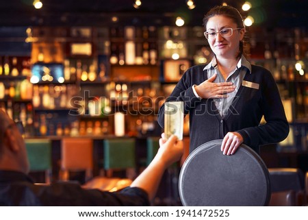 Waitress takes the tip. The waiter female receives a tip from the client at the hotel bar. The concept of service Royalty-Free Stock Photo #1941472525