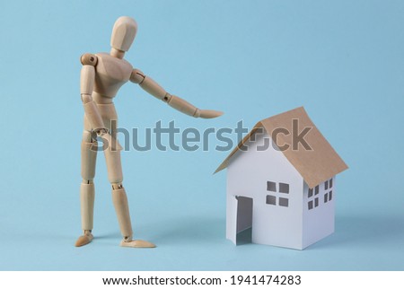 Home sale concept. Puppet realtor points to a house figurine on a blue background