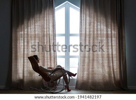 Woman sitting in a rocking chair and looking in a window