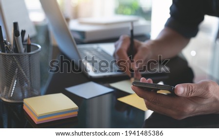 Business man working, project planning work process, using mobile phone with laptop computer on office table. Young worker posting with notepad reminders creative brainstorming, startup business 