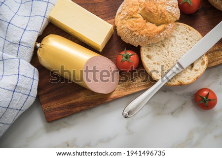 German fine veal liver sausage spread with crispy bread roll bun, butter, tomatoes and knife on wooden board, kitchen towel and light marble background for breakfast