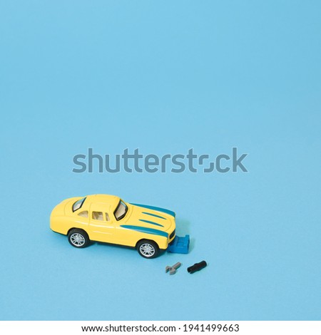 Metal toy yellow classic car and auto mechanic with tools. Blue background. Minimal composition.